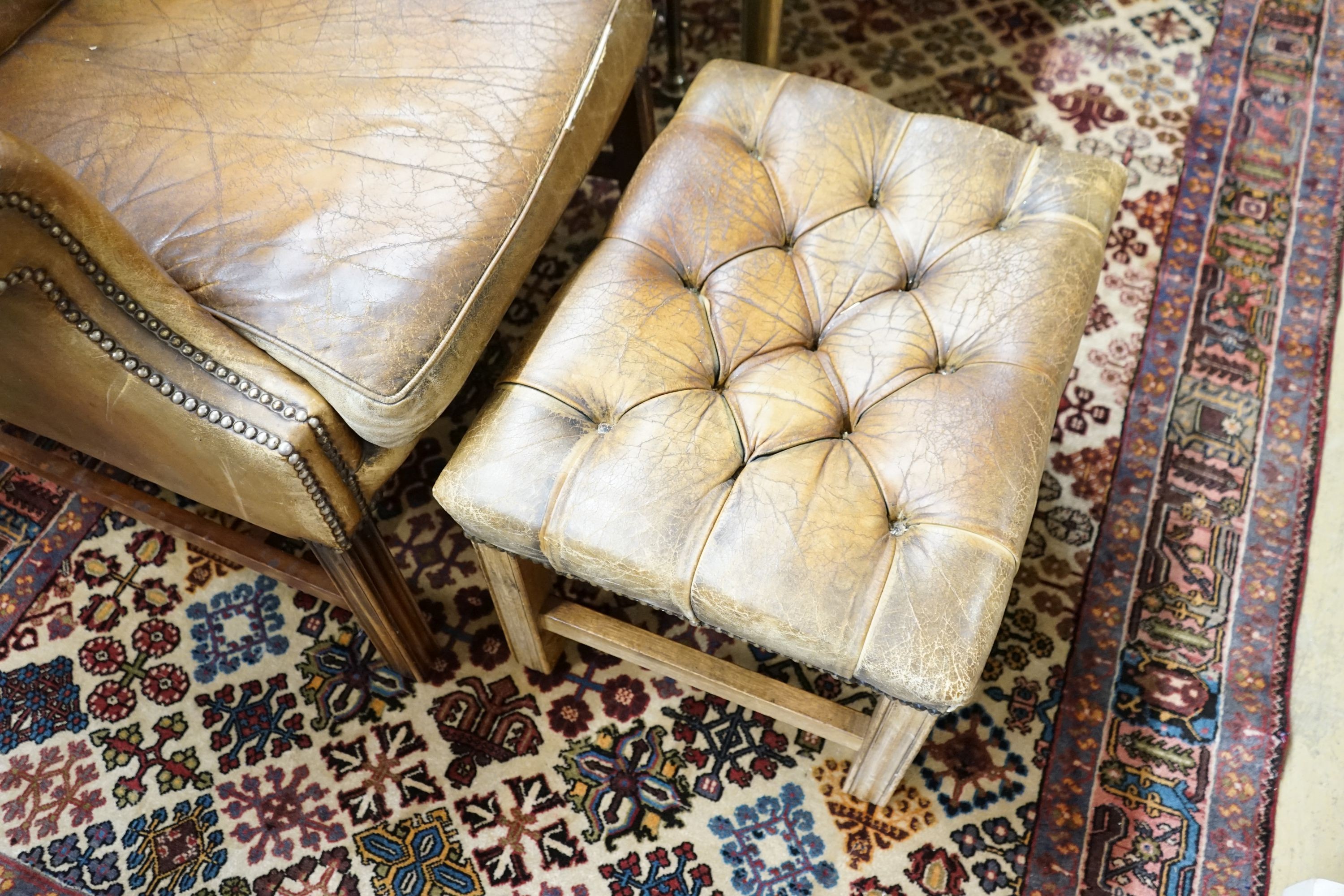 A leather wing armchair upholstered in buttoned brown leather, width 82cm, depth 77cm, height 110cm together with a similar foot stool